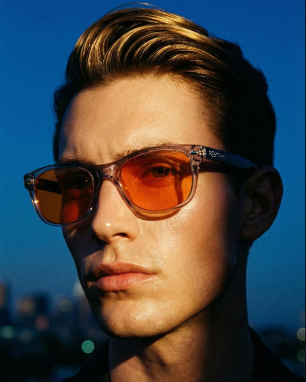 Man wearing orange-tinted sunglasses with a blurred cityscape background